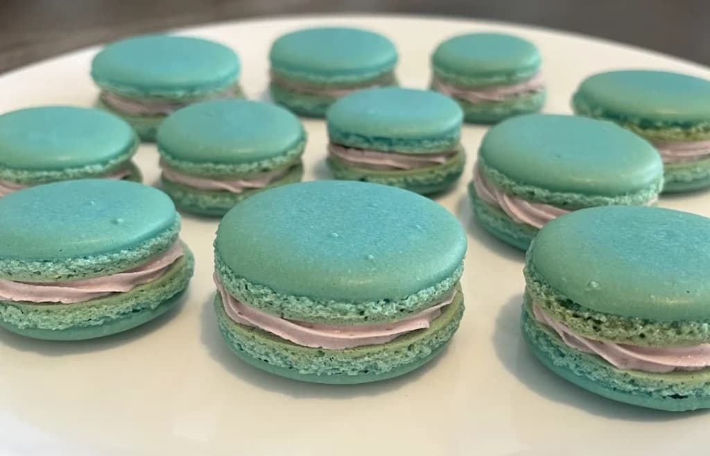 A plate of homemade teal macarons sandwiched with pink raspberry buttercream
